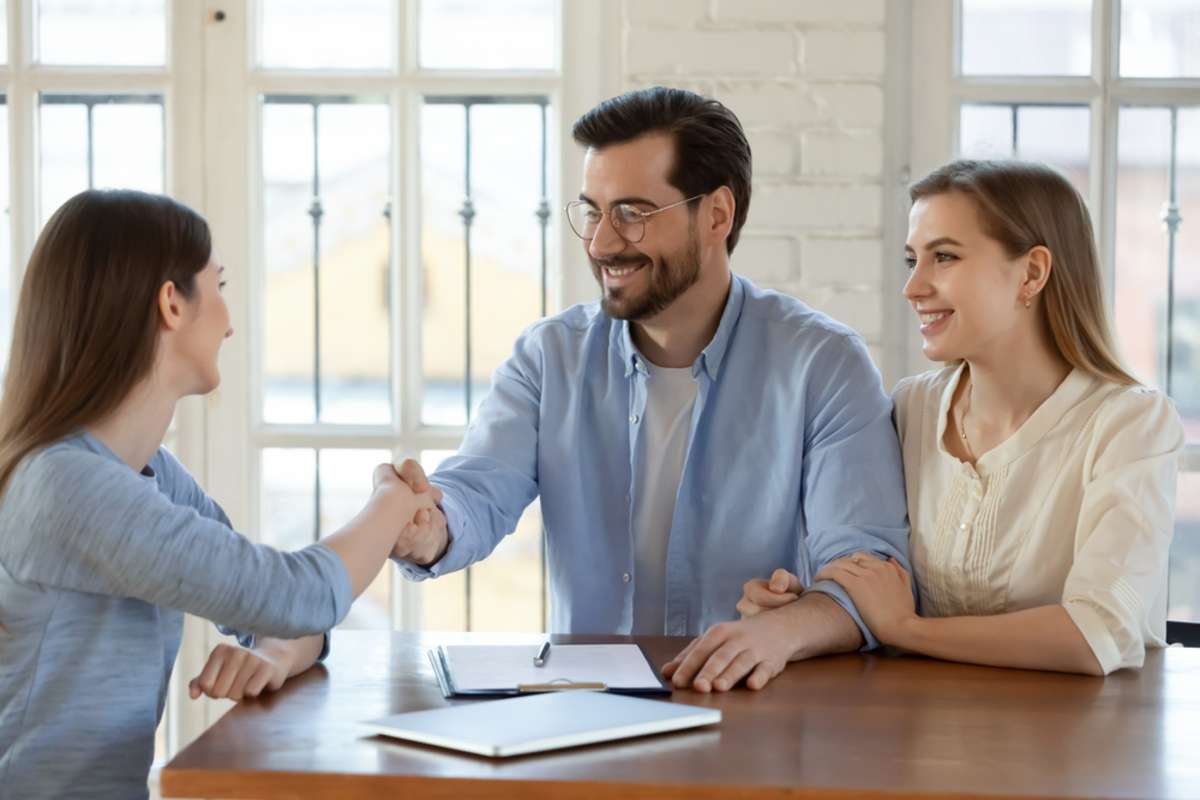 Happy young married family couple shaking hands with real estate agent