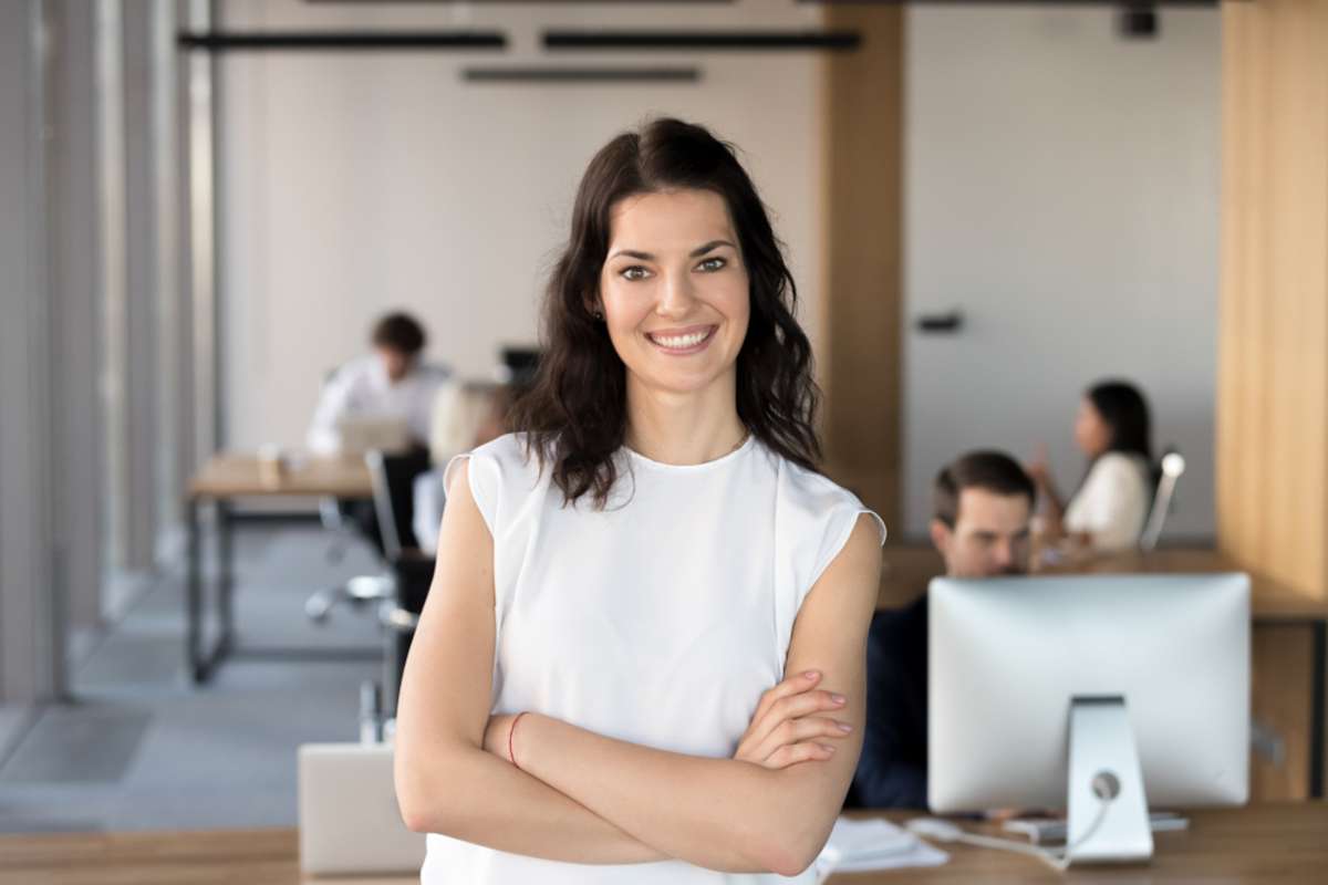 Head shot portrait of successful smiling businesswoman with arms crossed standing in office