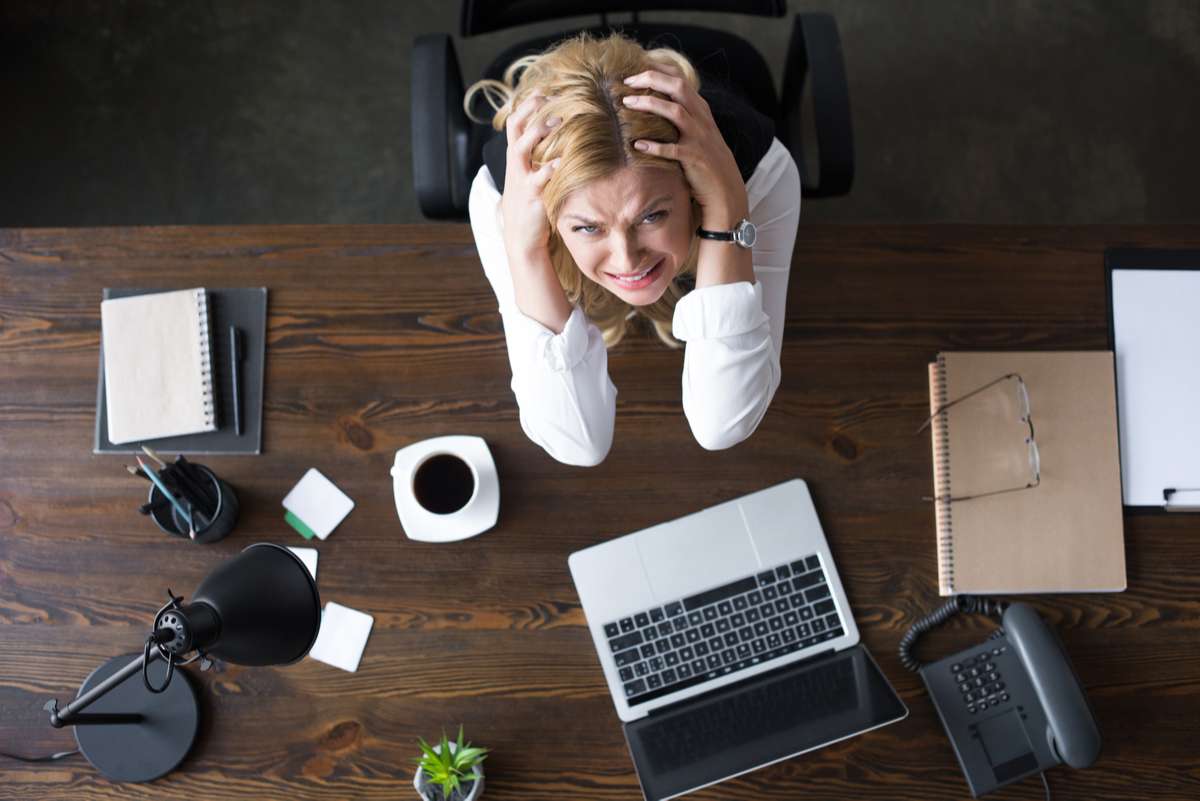 Overhead view of stressed businesswoman touching head with hands and looking at camera in office