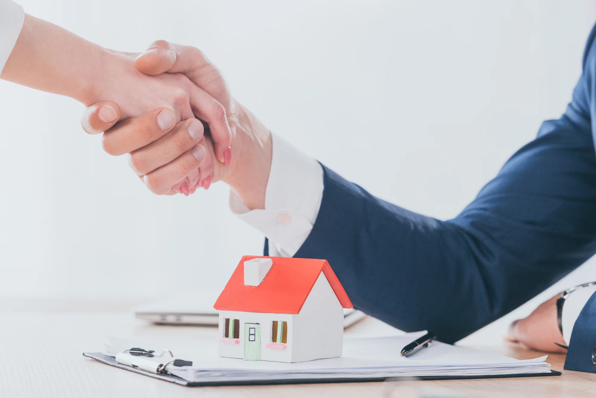 Partial view of realtor shaking hands with customer near house model on tabletop
