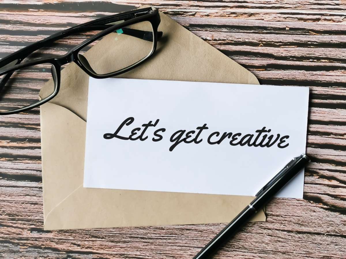 Text lets get creative written on white paper with a pen,brown envelope and eye glasses