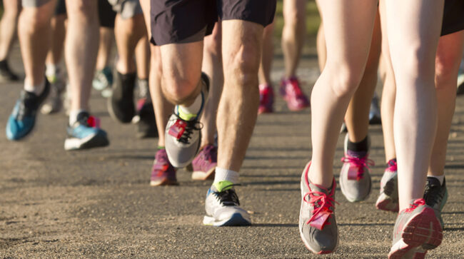 Legs of runners on a dirt path next to a lake running 5K